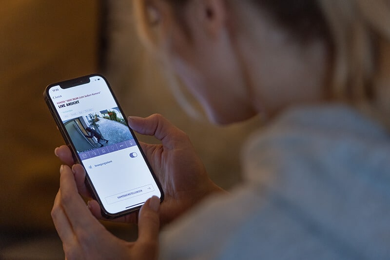 Person betrachtet das Livebild einer Überwachungskamera auf einem Smartphone.