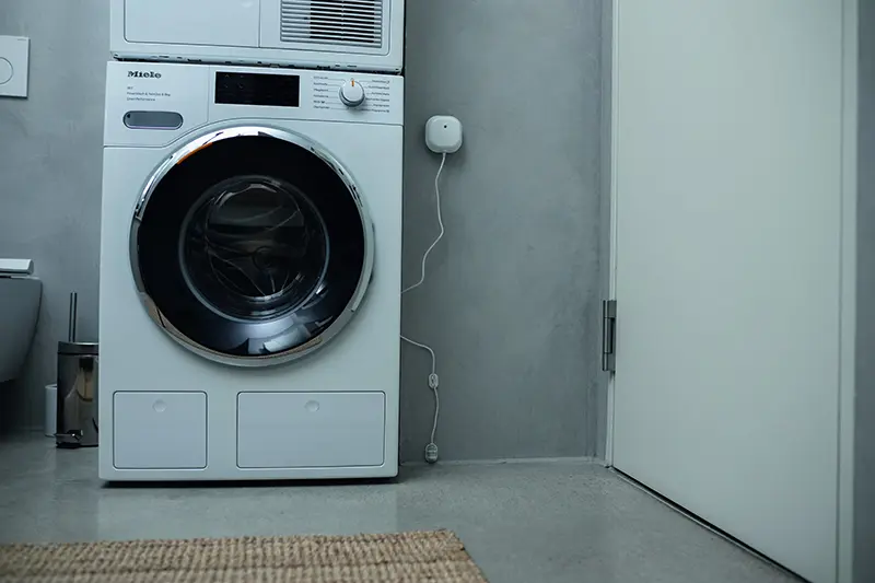 Waschmaschine in einem Hauswirtschaftsraum mit Wassermelder an der Wand